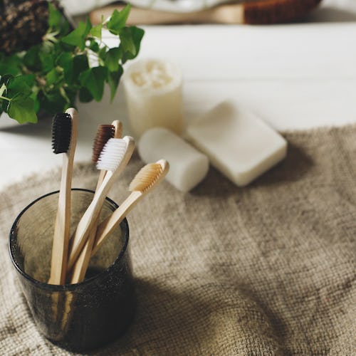 eco natural bamboo toothbrushes in glass on rustic background with greenery. sustainable lifestyle c...
