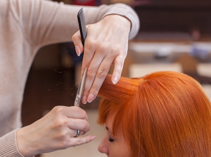 The hairdresser does a haircut with scissors of hair to a young with red hair girl in a beauty salon...