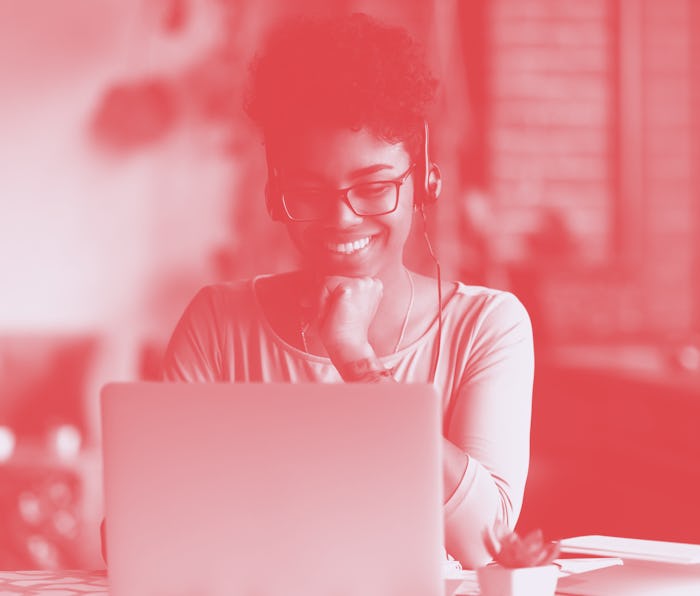 A woman smiles and looks at her laptop with headphones on.