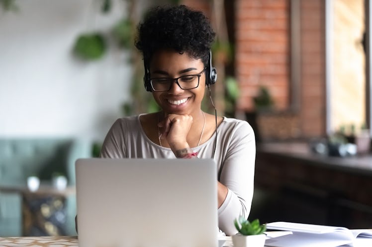 A woman smiles and looks at her laptop with headphones on.