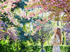 A woman wearing a white and black dress admires the cherry blossoms outside on a spring day. 