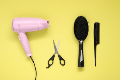 Pink hair dryer black brush, comb and scissors on yellow paper background