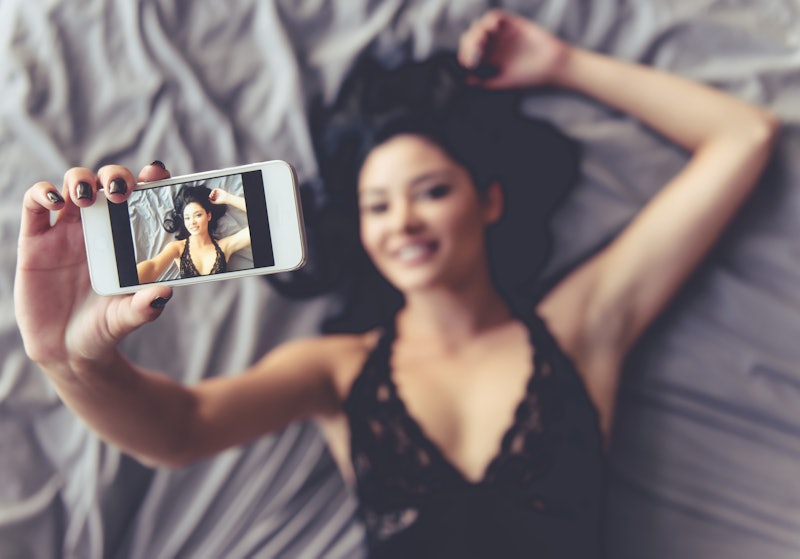 Top view of sensual young woman in black lingerie making selfie using a smartphone and smiling while...