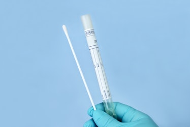 Lab technician holds culture swab and tube with blue background.