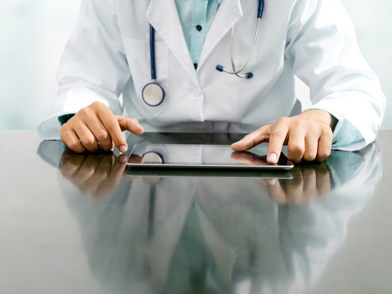 Male doctor sitting at table with tablet computer in hospital office. Medical healthcare staff and d...
