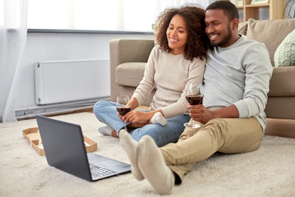 A couple relaxes at home, drinking wine, while watching a virtual wine tasting on their computer. 