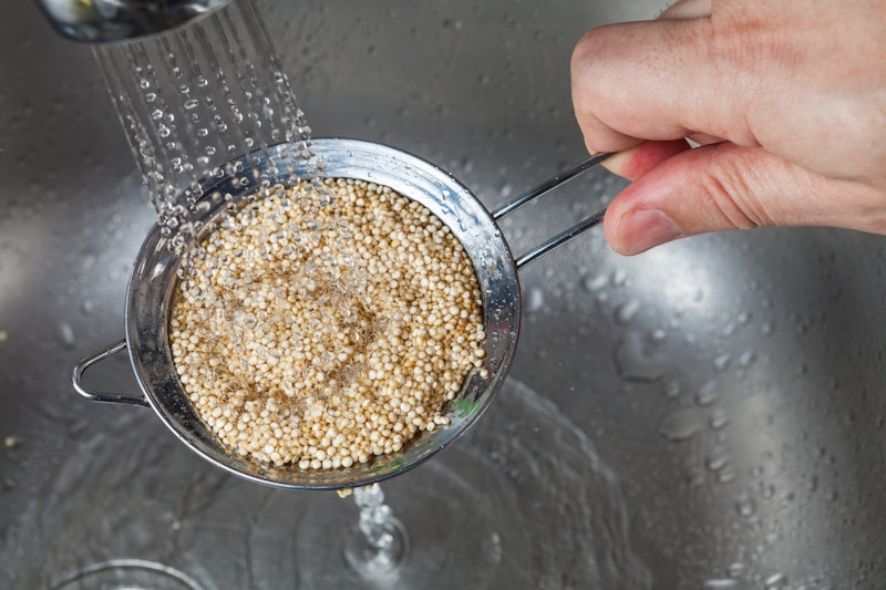 Man holding small strainer with raw quinoa seeds and rinsing it in cold water in the kitchen sink