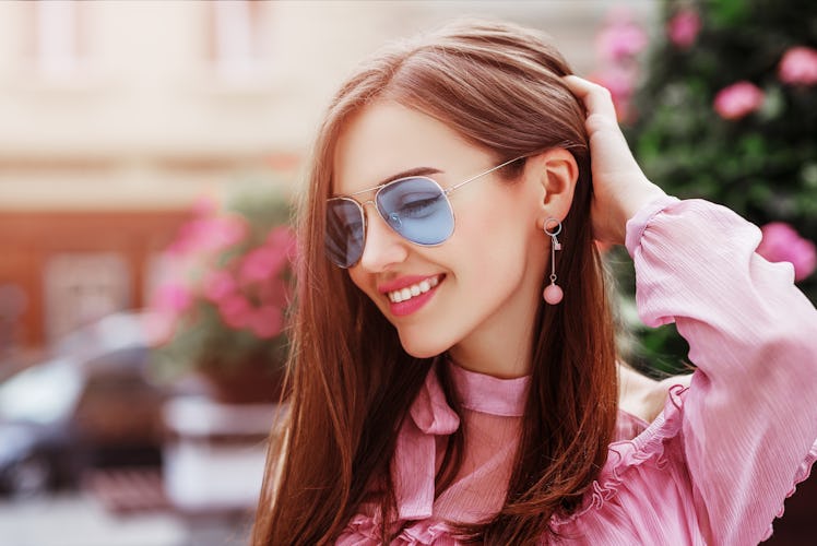 Outdoor close up portrait of young beautiful happy smiling woman wearing blue aviator sunglasses, tr...