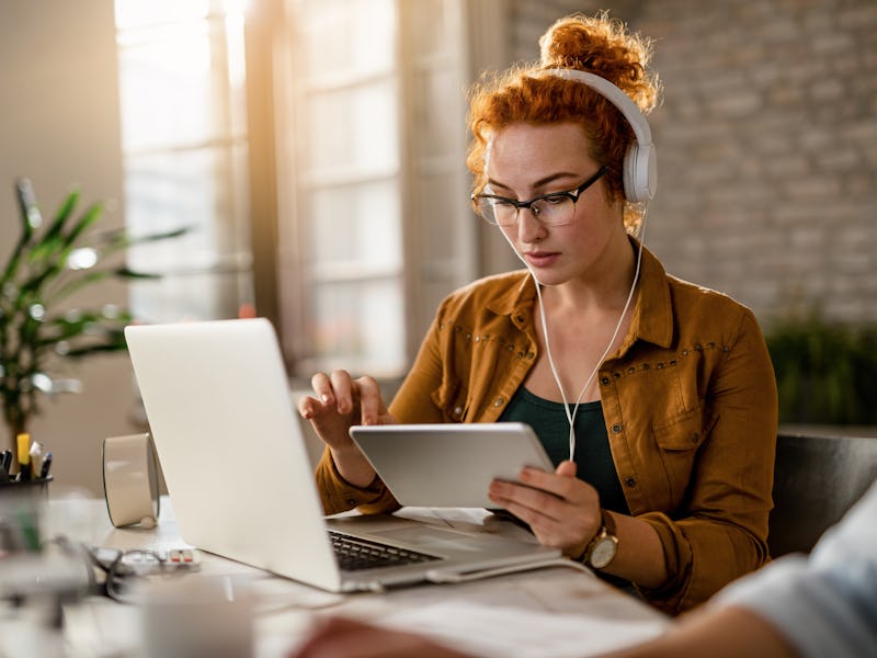 Young creative businesswoman working on digital tablet while wearing headphones in the office.