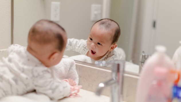 Adorable 4 month old asian baby boy in looking into bathroom mirror, ready for bath