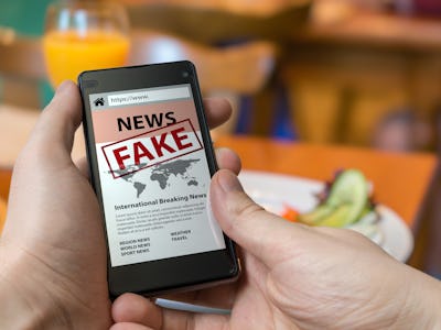 Man is holding smartphone and reading fake news on internet. Propaganda, disinformation and hoax con...
