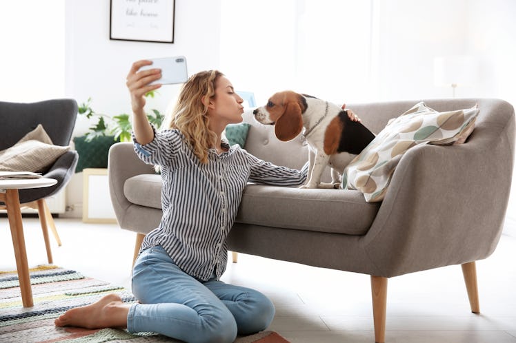 A woman goes in for a kiss, while taking a selfie with her dog at home.