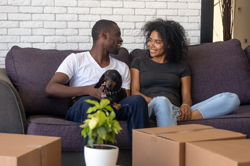 Young african american couple happy to move into new home with pet and boxes, black family tenants c...