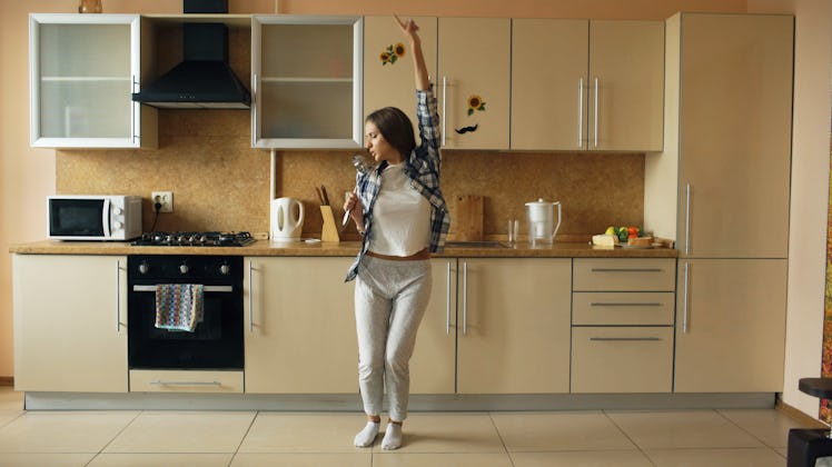 A woman in sweats dances in her bright kitchen.