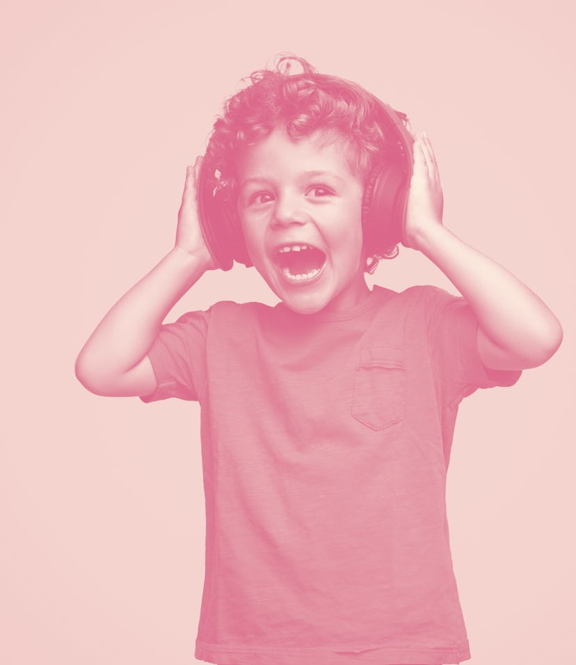 Screaming excited curly kid in headphones listening to music on blue background 