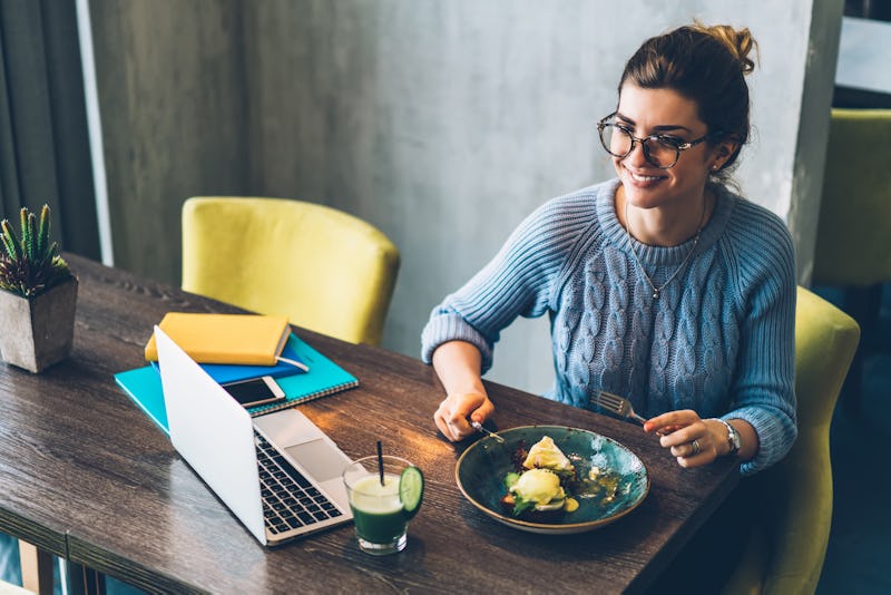 Positive young woman freelancer in eyeglasses watching funny video on website on modern laptop compu...