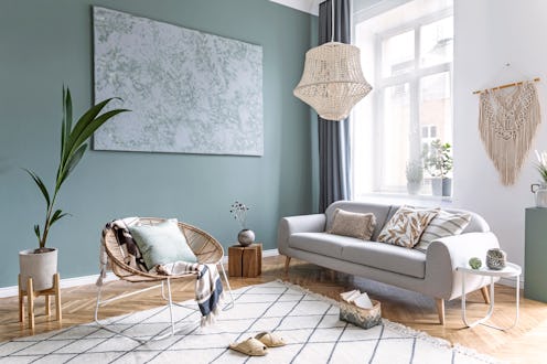 Stylish and design composition of living room with gray sofa, rattan armchair, cube, plaid, pillows,...