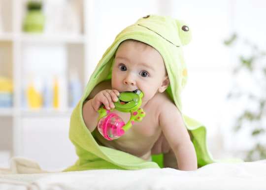 Baby boy with green towel after the bath biting toy.