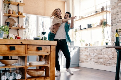A trendy couple laughs and dances in a bright kitchen.
