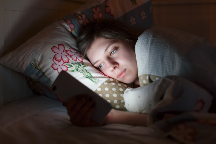 Young sleepy tired girl lying in bed using smartphone at late night, can not sleep. Social media add...