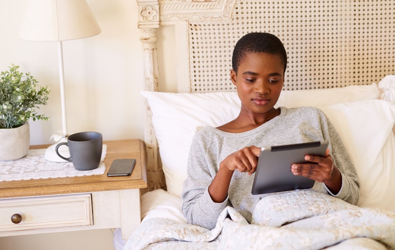 Young African American woman relaxing in her bed in the morning using a digital tablet