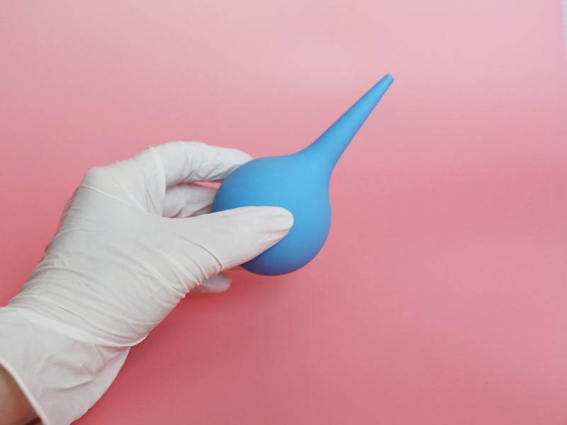 Blue syringe with a soft tip in the female hand of a doctor. A hand in a latex glove holds an enema....