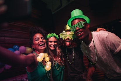 A group of friends smiles for a selfie and celebrates St. Patrick's Day at a bar.