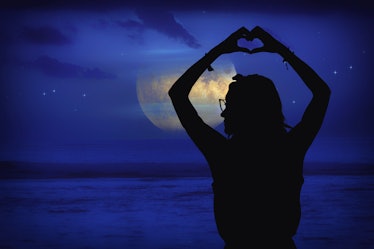 Silhouette of a girl at moonlit sky with stars near ocean holding heart - shape sign with hands. My ...