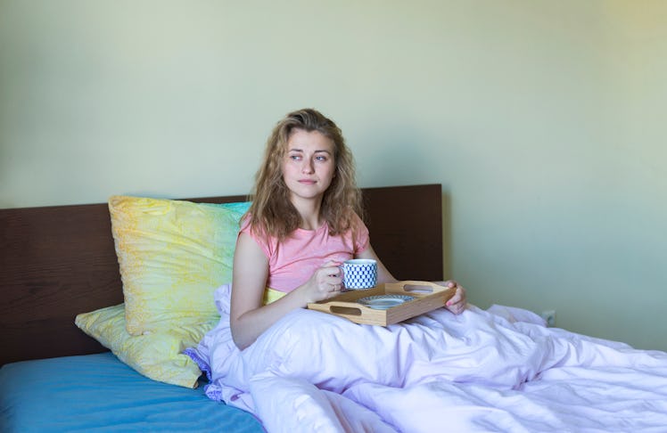 A woman relaxes with a cup of coffee in bed.