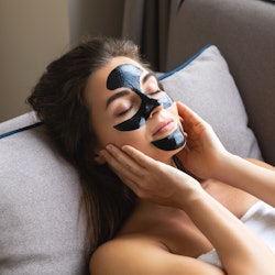 Young beautiful woman is relaxing at home with applied black peel-off mask on her face