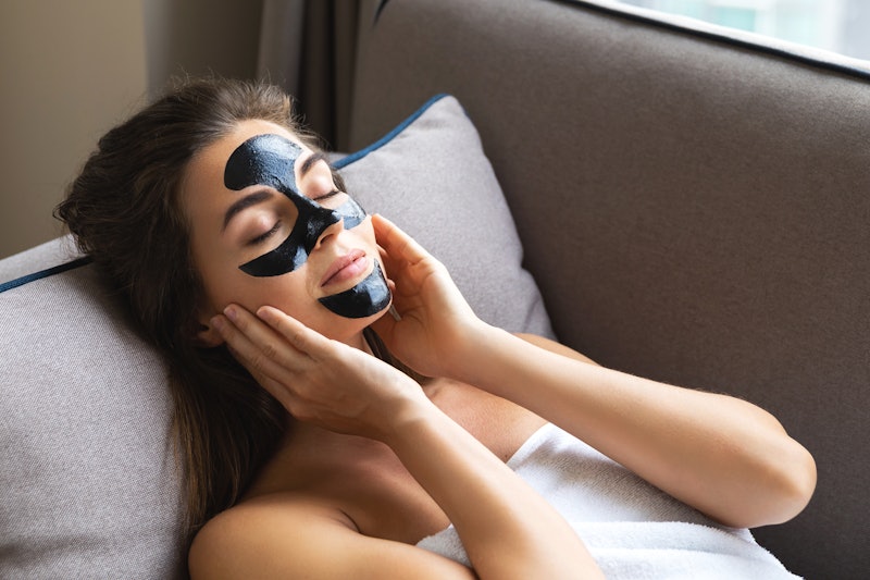 Young beautiful woman is relaxing at home with applied black peel-off mask on her face