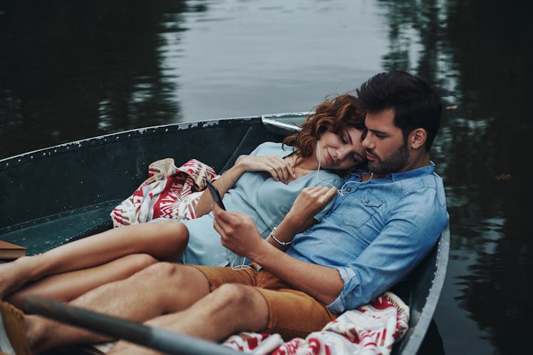 A couple relaxes in a rowboat, listening to music.