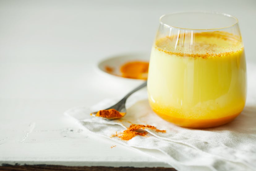 Healthy ayurvedic drink golden almond milk or pumpkin turmeric latte with curcuma powder on white ba...