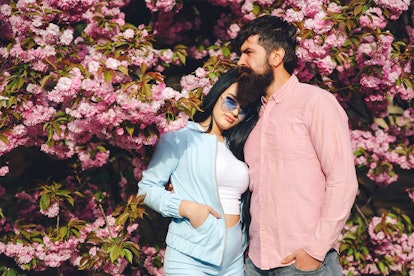 A woman wearing all blue holds onto her partner in pink, while standing in front of spring cherry bl...