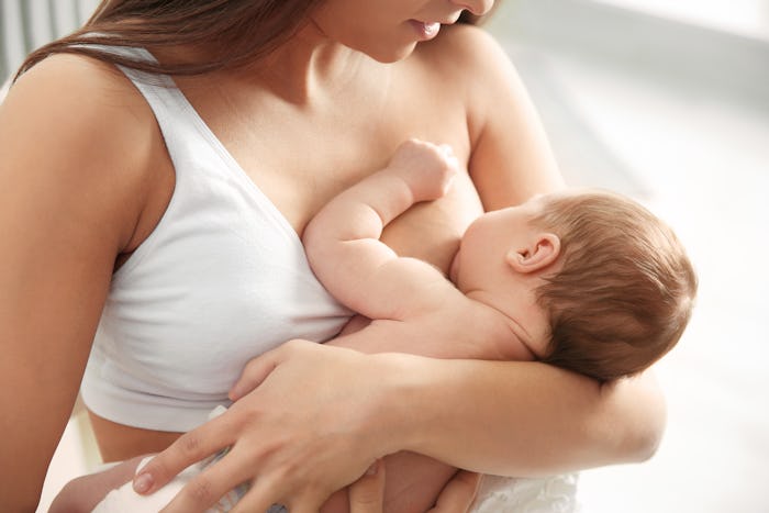 Young woman breastfeeding her baby on blurred background, closeup