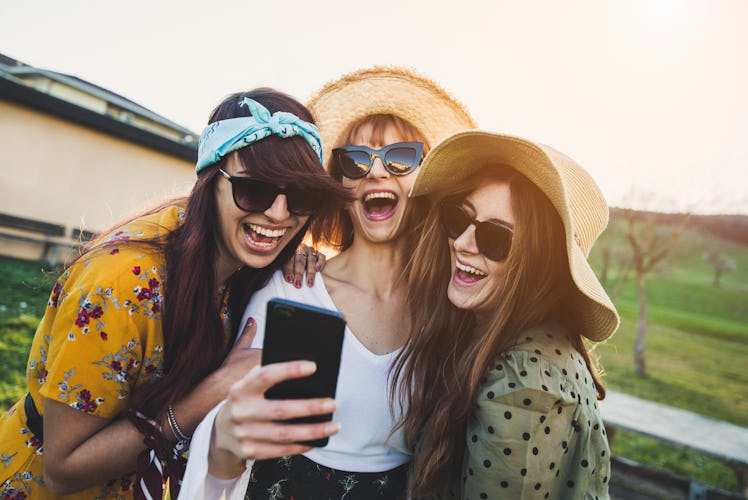 Happy millennials girls laughing and messaging on a smartphone outdoor. Three women having fun smili...
