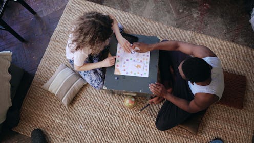 Top view of multiracial couple sitting on floor and playing board game. Woman throws dice, takes car...