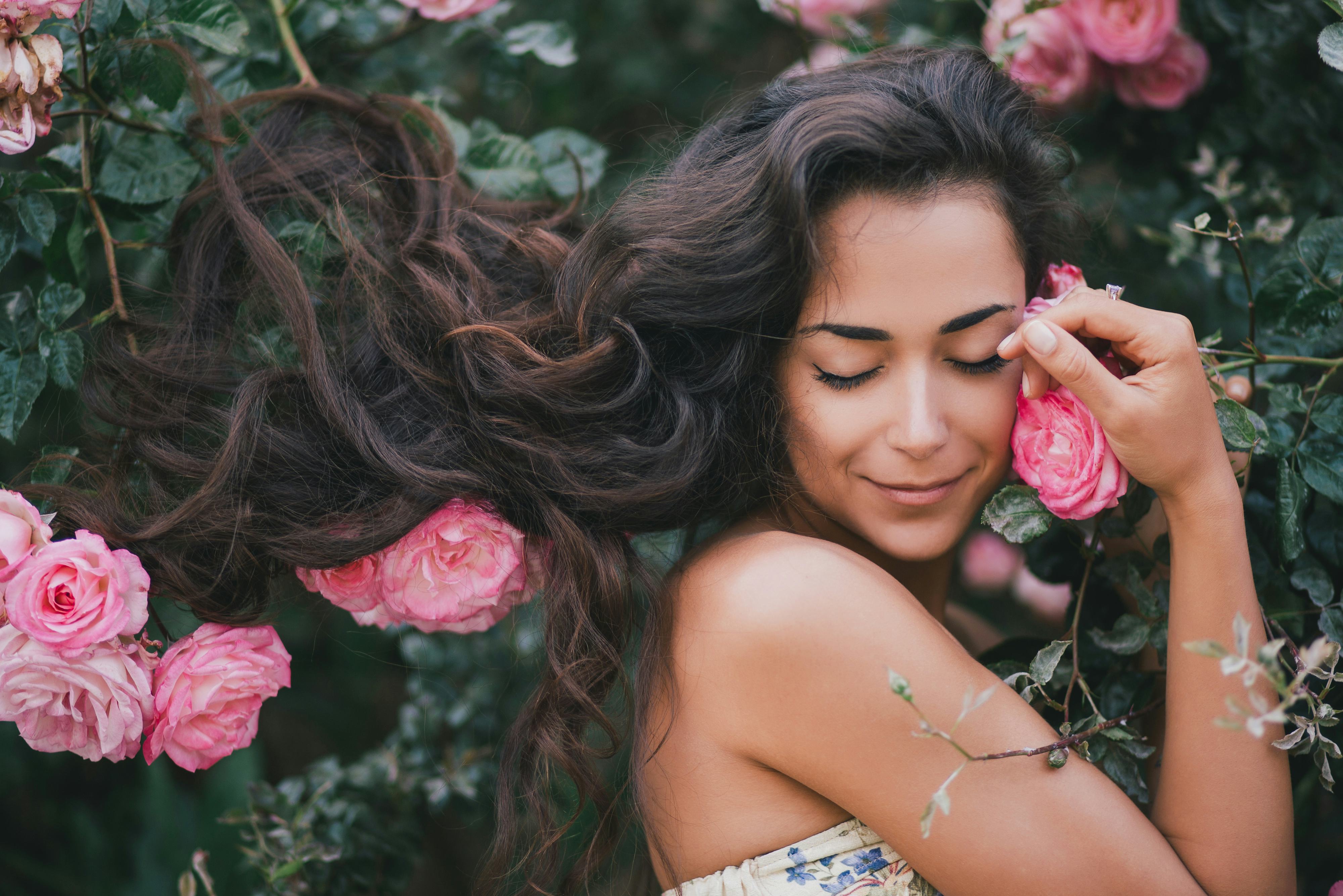 Beautiful young woman with long curly hair posing near roses in a garden
