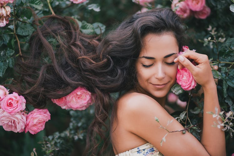 Beautiful young woman with long curly hair posing near roses in a garden