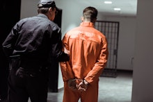 rear view of prison officer leading prisoner in handcuffs in corridor