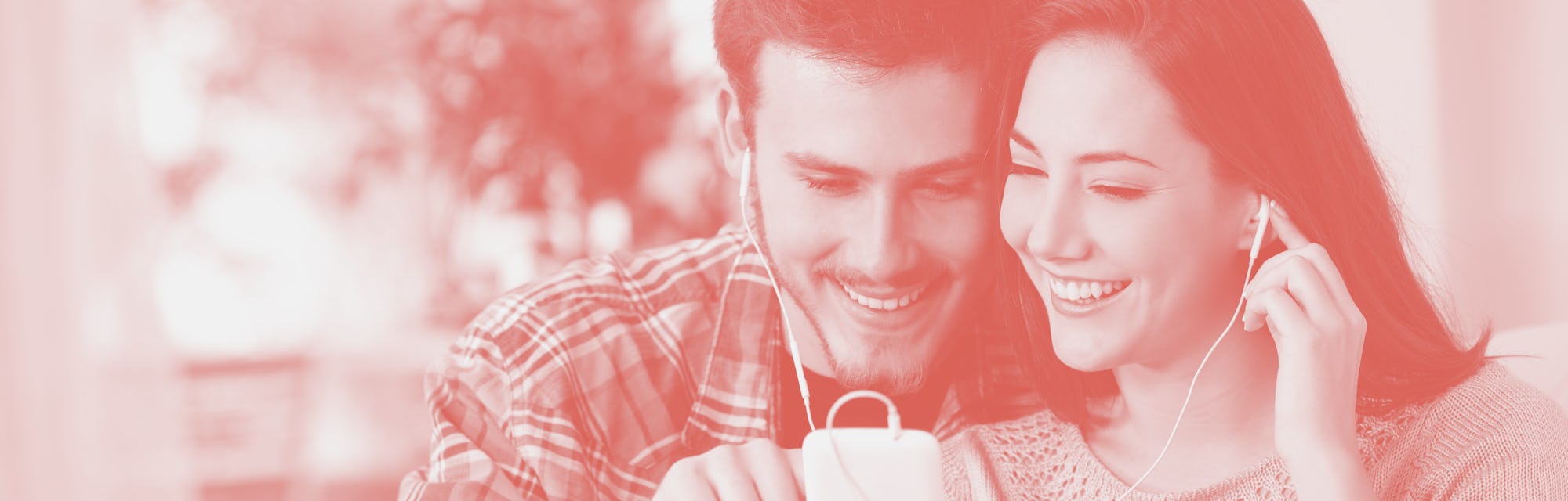 Happy couple sharing music from smart phone sitting on a couch at home