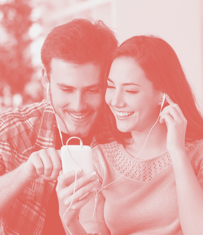 Happy couple sharing music from smart phone sitting on a couch at home