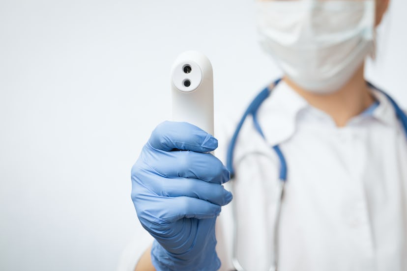 Close-up shot of doctor wearing protective surgical mask ready to use infrared forehead thermometer ...
