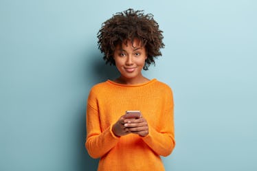 Isolated shot of positive smiling woman holds modern cellular, enjoys wireless internet, checks bank...