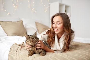 pets, comfort, christmas, winter and people concept - happy young woman with cat lying in bed at hom...