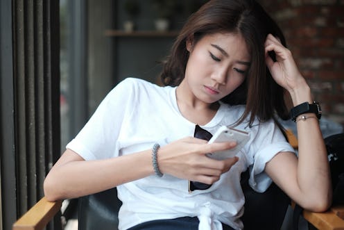 Asian girl sitting in coffee shop playing mobile phone for social media on vacation time, girl relax...
