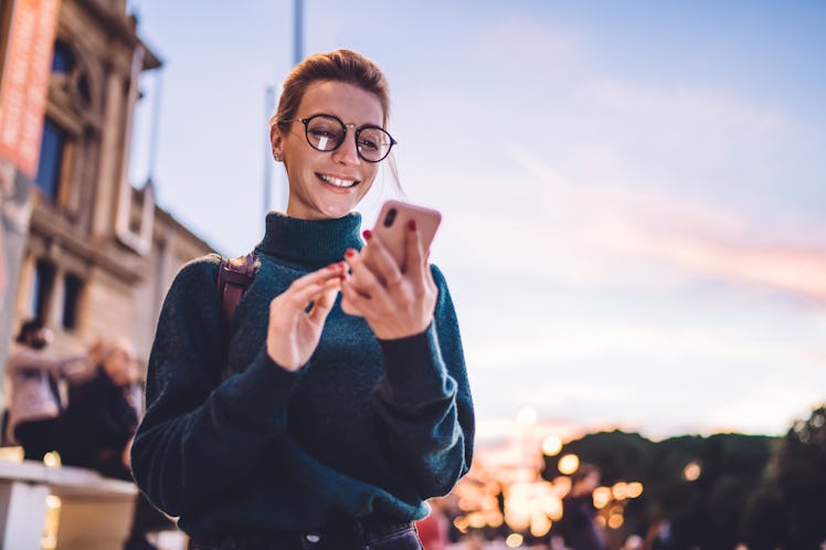 A young woman texts her crush a question while on a walk outside.