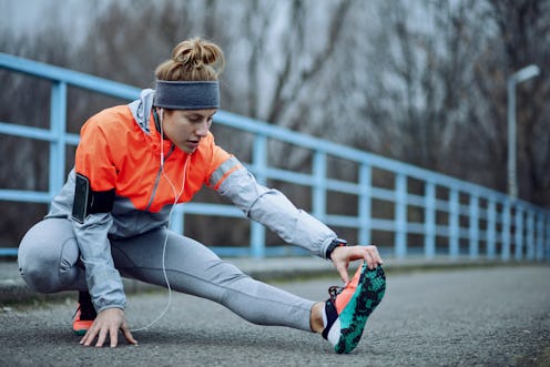 Young athletic woman doing stretching exercises and preparing for sports training during cold weathe...