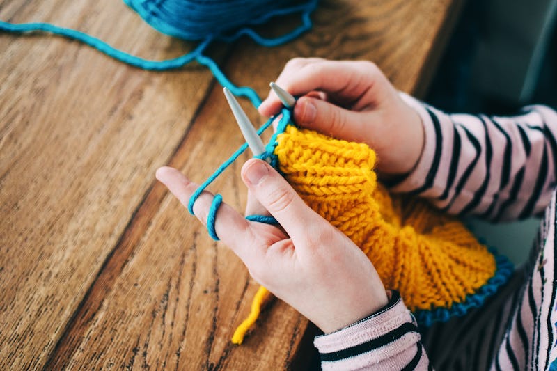 Young girl knitting a circle scarf with yellow and blue coloured yarn. Sitting at the wooden table, ...