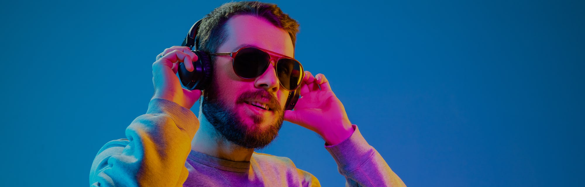 Enjoying his favorite music. Happy young stylish man in hat and sunglasses with headphones listening...